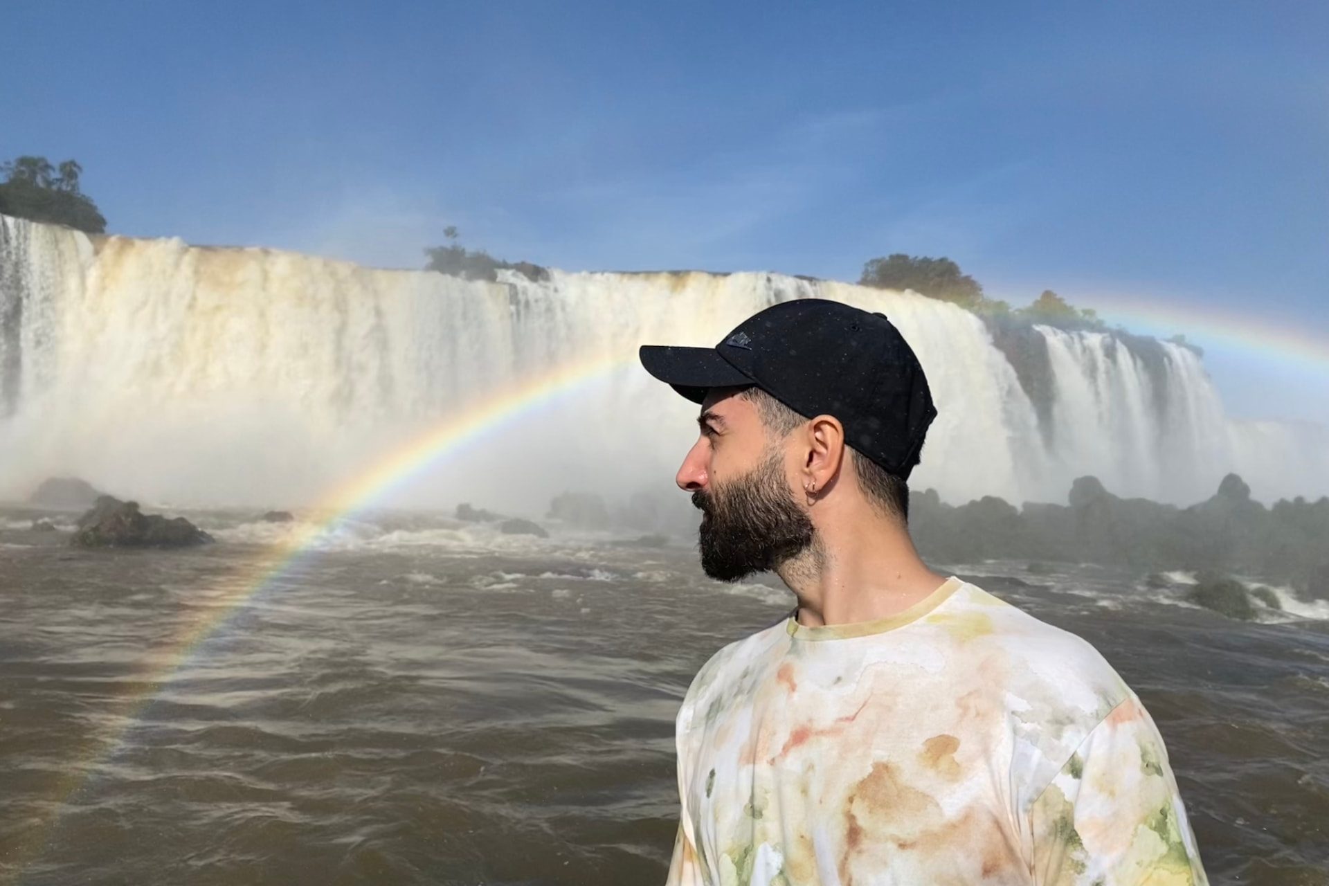 Tunay Guer vor einem Wasserfall mit Regenbogen